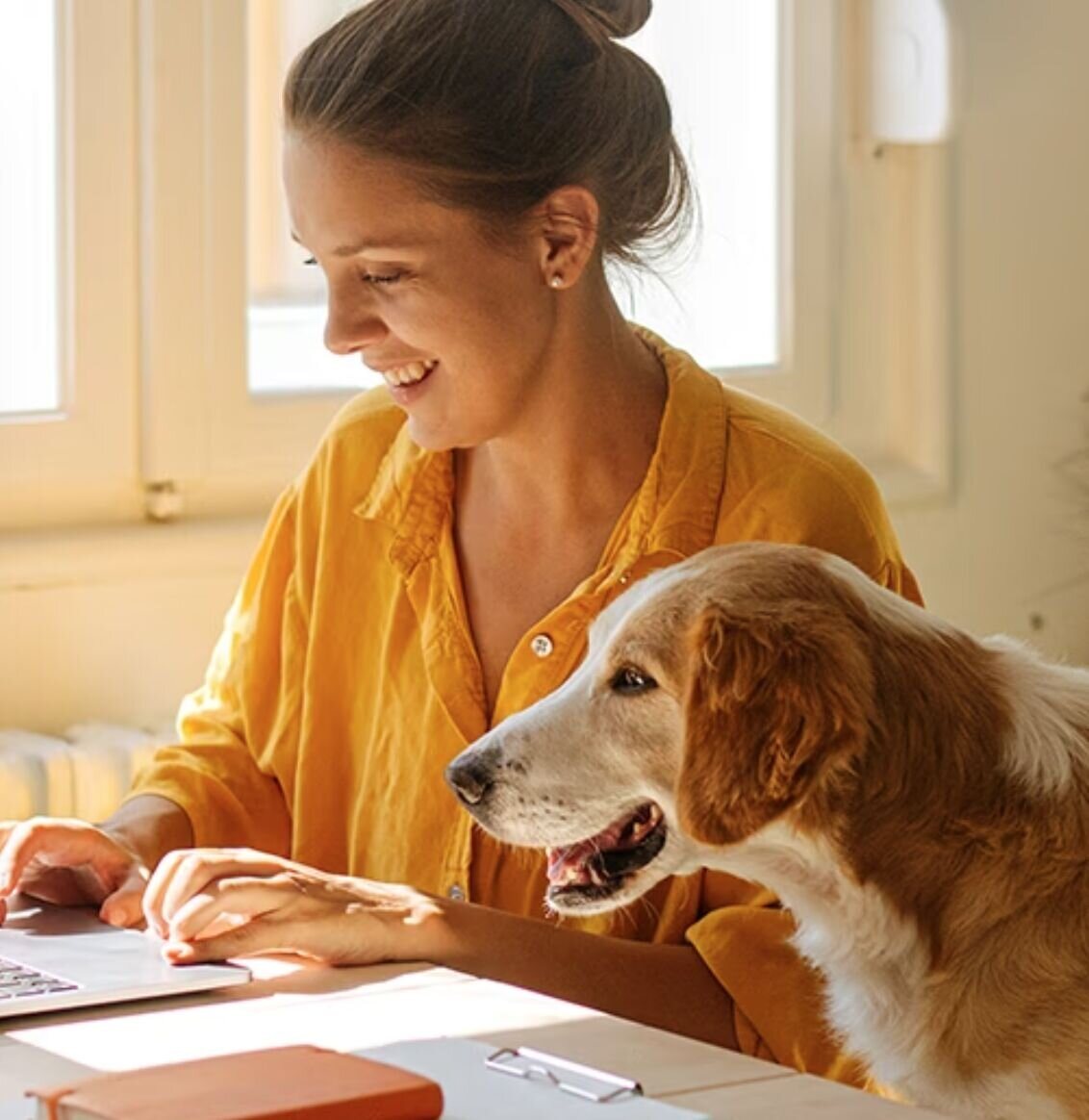 Une femme sourit devant son ordinateur, son chien à ses côtés
